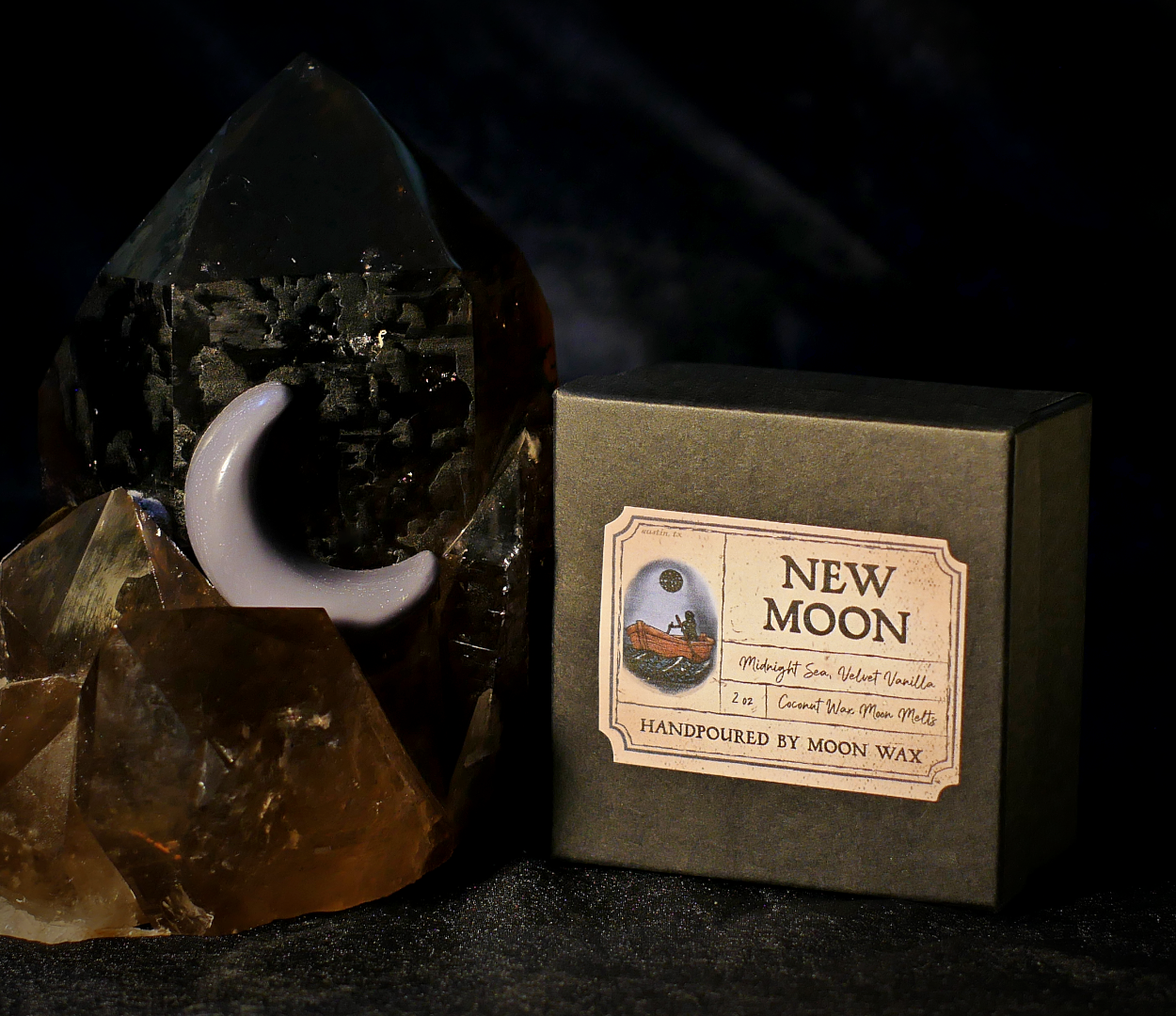 Box of 'New Moon' wax melts with a crystal and moon-shaped wax melt on a dark background