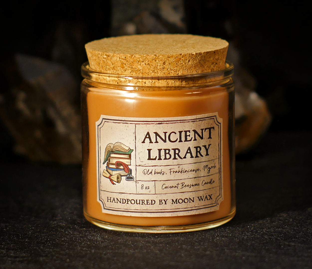 Ancient Library Candle in a clear corked jar with dark-brown colored coconut beeswax and apothecary inspired label on a dark background. The label reads Old Books, Frankincense, Myrrh, 8 ounces, and hand poured by Moon Wax.