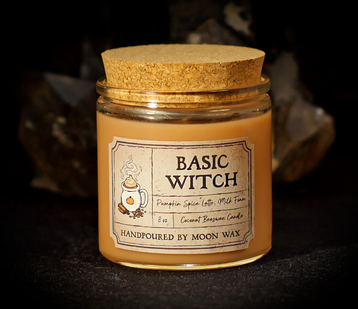 Basic Witch Candle in a clear corked jar with brown colored coconut beeswax and apothecary inspired label on a dark background. The label reads Pumpkin Spice Latte, Milk Foam, 8 ounces, and hand poured by Moon Wax.