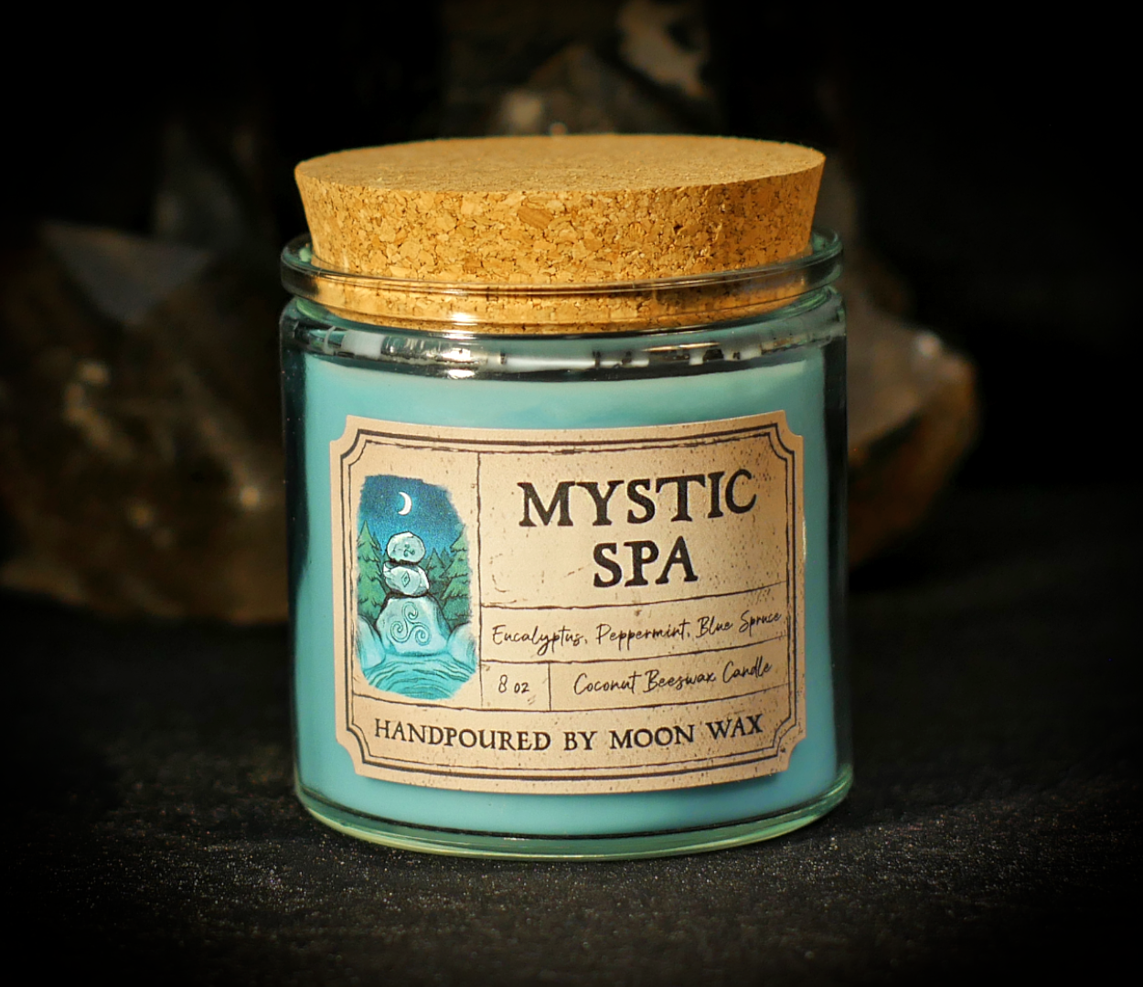 Mystic Spa Candle in a clear corked jar with teal-blue colored coconut beeswax and apothecary inspired label on a dark background. The label reads Eucalyptus, Peppermint, Blue Spruce, 8 ounces, and hand poured by Moon Wax.